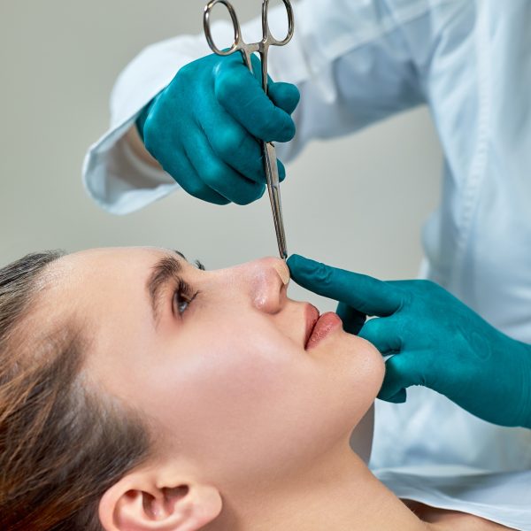 Lady with plaster on nose, doctor examining patients face after plastic surgery